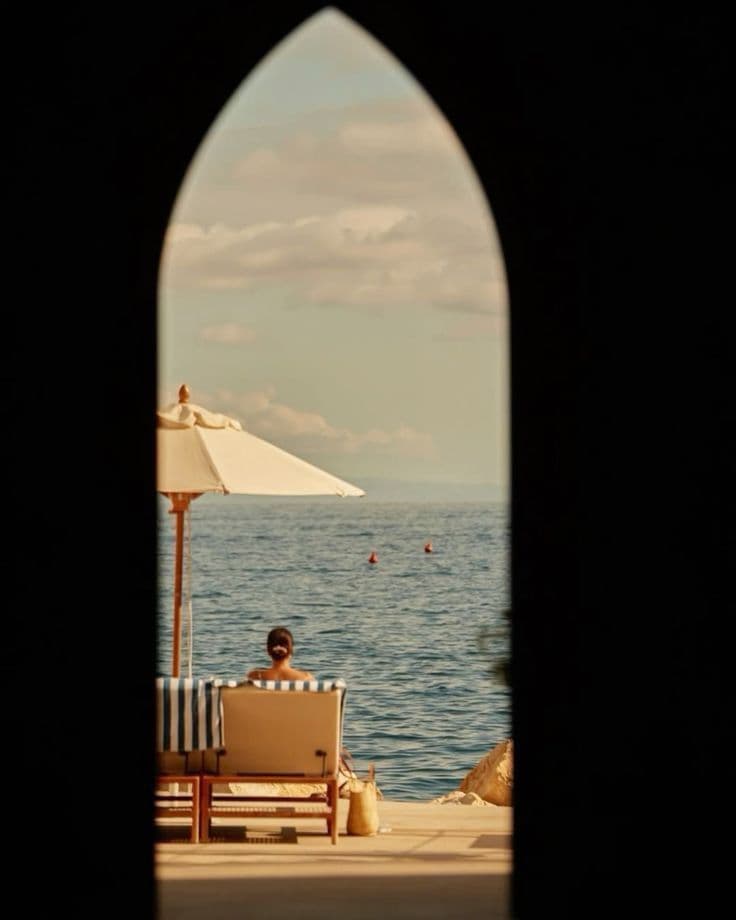 Guest on a sea-facing lounger viewed through an arched doorway